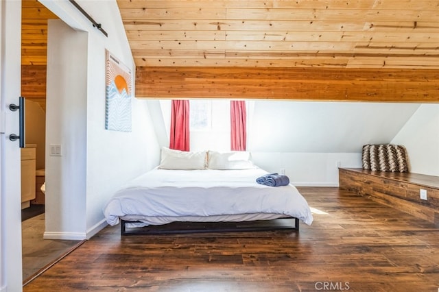 bedroom with lofted ceiling, a barn door, baseboards, and wood finished floors