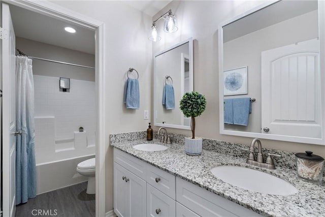 full bath with double vanity, a sink, toilet, and wood finished floors