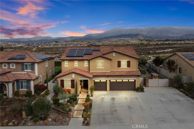 view of front of property with a mountain view, solar panels, fence, a gate, and stucco siding