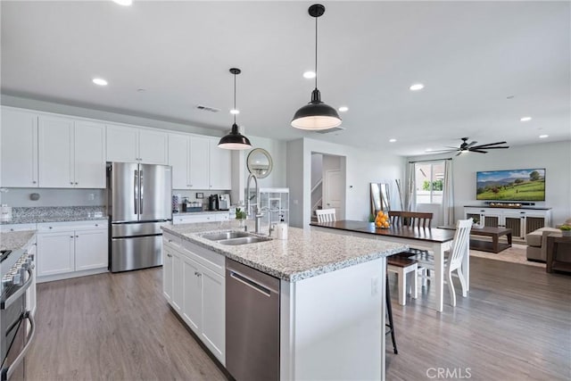 kitchen featuring open floor plan, stainless steel appliances, a sink, and light wood-style floors