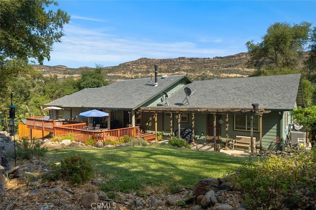 rear view of house with a deck with mountain view, a yard, and roof with shingles