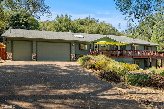 view of front of home with an attached garage, stone siding, driveway, and a deck