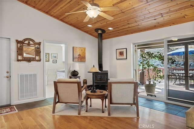 sitting room featuring wood finished floors, wood ceiling, visible vents, vaulted ceiling, and a wood stove