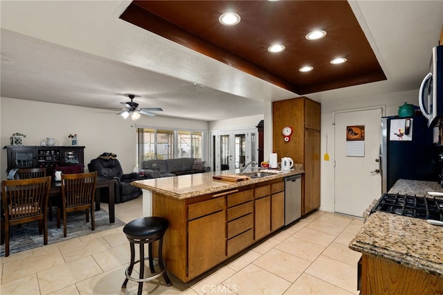 26131 Chambers Ave, Menifee, CA 92586 - kitchen featuring stainless steel appliances, brown cabinets, a raised ceiling, a peninsula, and a ceiling fan