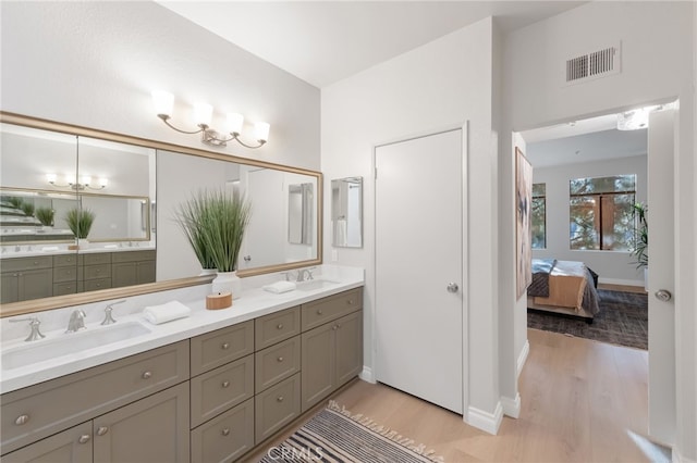 ensuite bathroom with double vanity, wood finished floors, a sink, and visible vents