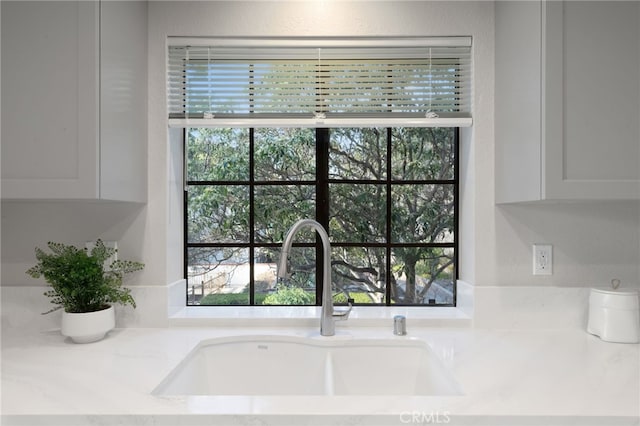 interior details with a sink, light stone countertops, and white cabinets