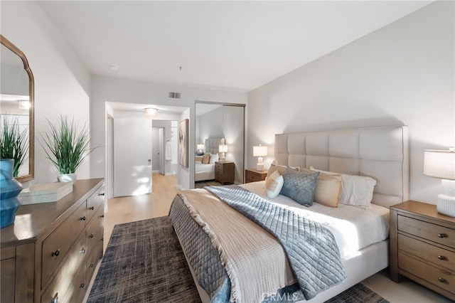 bedroom with light wood-type flooring, visible vents, and a closet