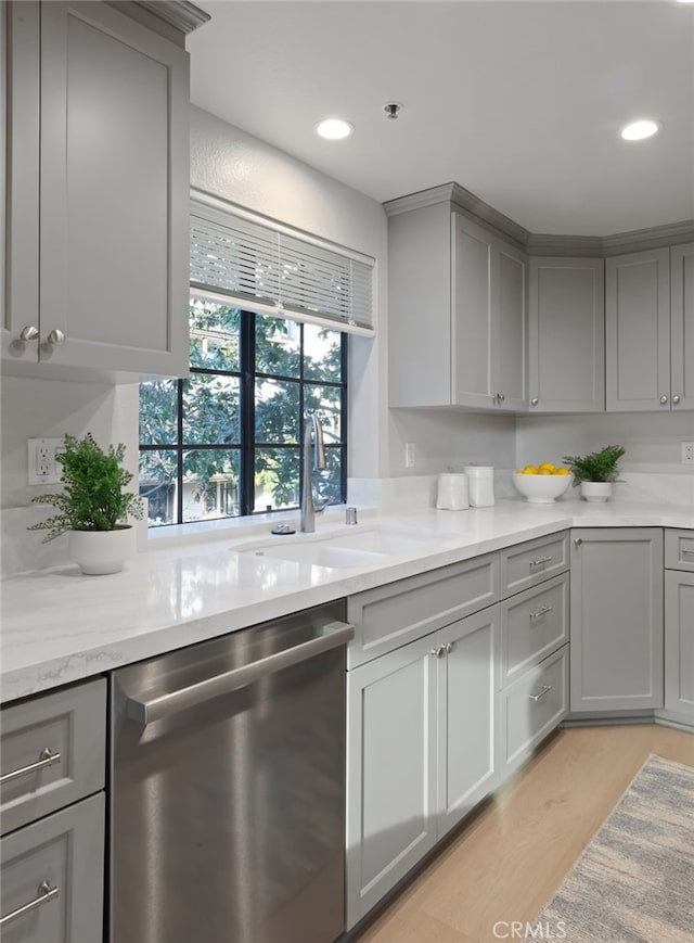 kitchen with stainless steel dishwasher, a sink, light wood-style flooring, and gray cabinetry