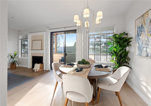 dining room featuring light wood-style floors, a fireplace, a notable chandelier, and baseboards