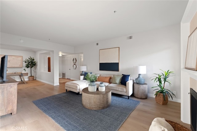 living room featuring visible vents, a fireplace, light wood-style flooring, and baseboards