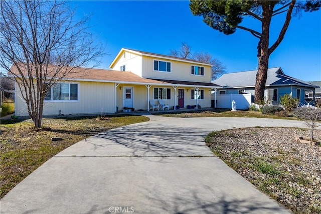 traditional home with concrete driveway, fence, and covered porch