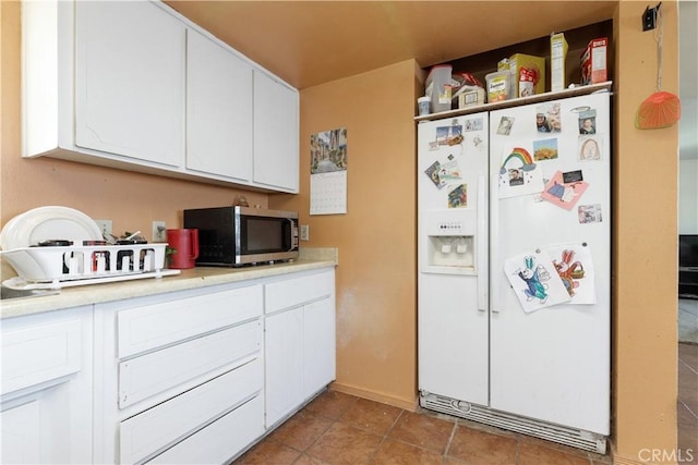kitchen with stainless steel microwave, light countertops, white refrigerator with ice dispenser, tile patterned floors, and white cabinetry