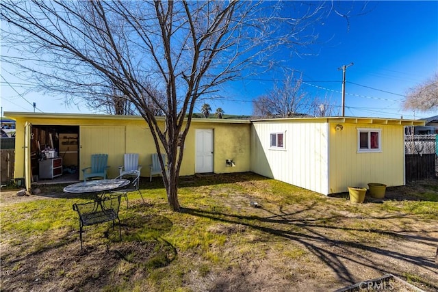 back of house featuring a lawn, an outdoor structure, and fence