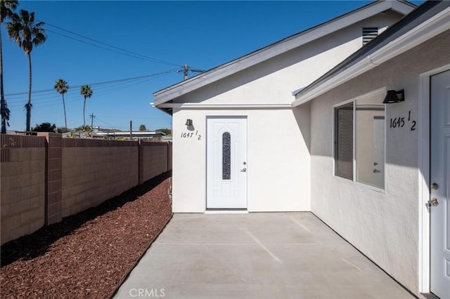 doorway to property with fence, a patio, and stucco siding