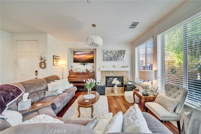 living area with a chandelier, wood finished floors, a fireplace with flush hearth, and visible vents