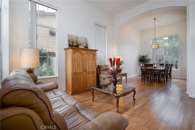 living room featuring light wood-style flooring, baseboards, arched walkways, and a wealth of natural light