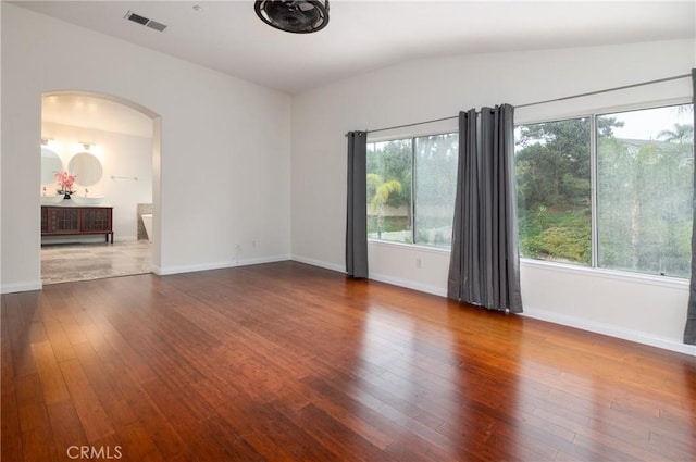 spare room featuring wood finished floors, baseboards, visible vents, lofted ceiling, and arched walkways