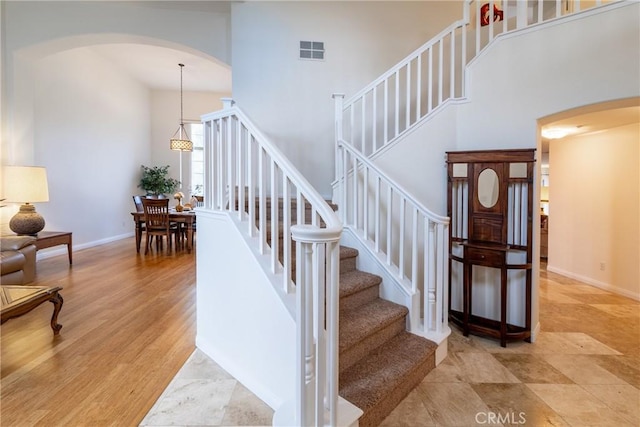 staircase featuring visible vents, wood finished floors, arched walkways, a high ceiling, and baseboards