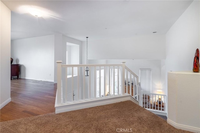 hallway featuring wood finished floors, an upstairs landing, and baseboards