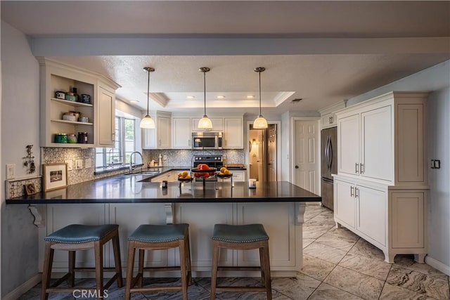 kitchen with a raised ceiling, a peninsula, marble finish floor, stainless steel appliances, and a sink