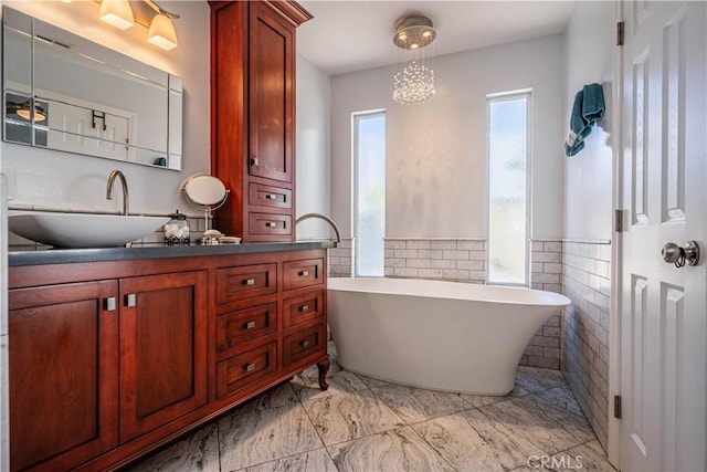 bathroom with tile walls, a soaking tub, marble finish floor, and vanity