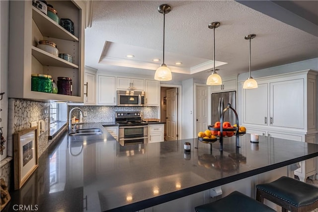 kitchen featuring a tray ceiling, tasteful backsplash, dark countertops, appliances with stainless steel finishes, and a sink