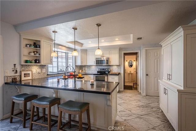 kitchen with dark countertops, a breakfast bar area, stainless steel appliances, and a raised ceiling