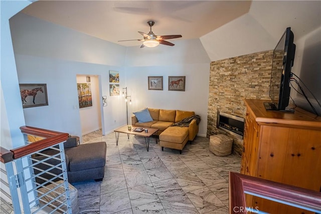 living area with a ceiling fan, marble finish floor, vaulted ceiling, and a stone fireplace