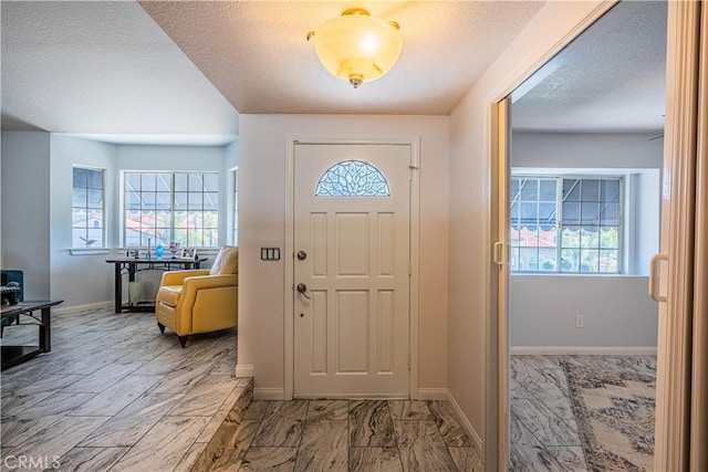 foyer entrance with marble finish floor, a textured ceiling, and baseboards