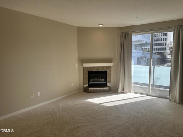 unfurnished living room featuring a fireplace with raised hearth, carpet floors, and baseboards