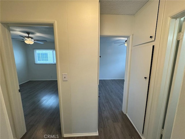 hall with a textured ceiling, dark wood-style floors, and baseboards