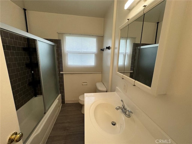 bathroom featuring toilet, shower / bath combination with glass door, wood finished floors, vanity, and baseboards