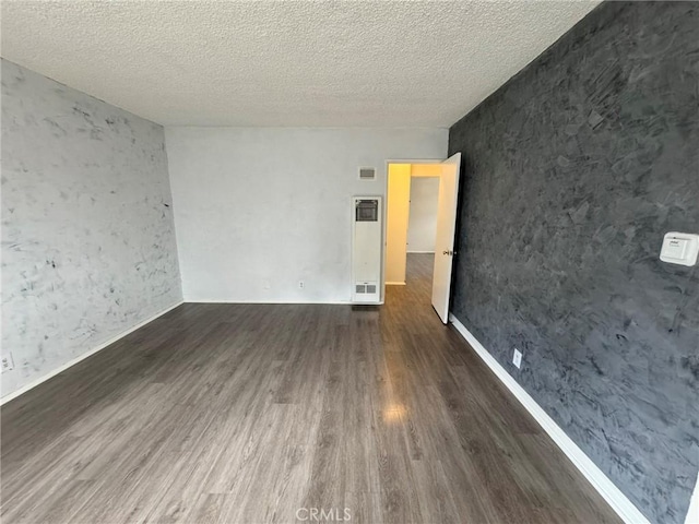 empty room featuring dark wood-type flooring, visible vents, and a textured ceiling