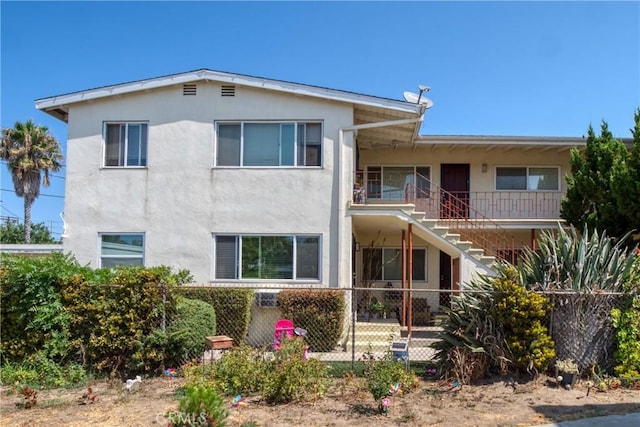 back of property featuring stairway, fence, and stucco siding