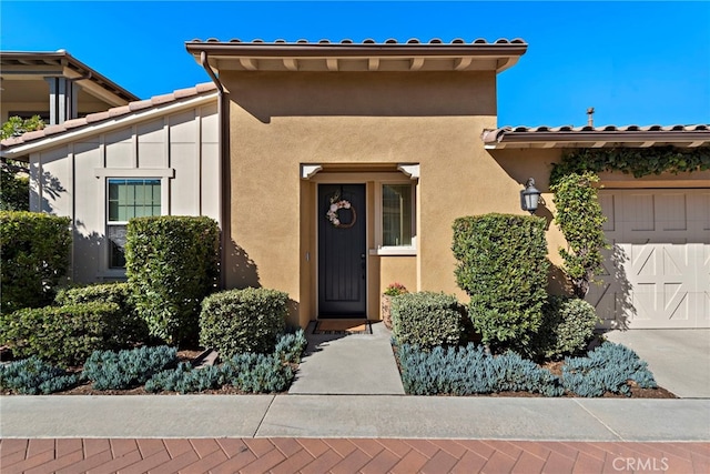 entrance to property with a garage, a tile roof, and stucco siding