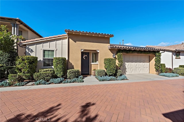 mediterranean / spanish home with decorative driveway, an attached garage, a tile roof, and stucco siding