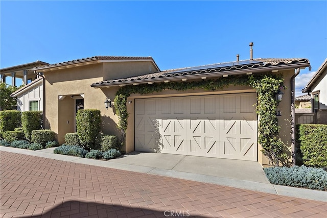 view of front facade with decorative driveway, a tile roof, an attached garage, and stucco siding