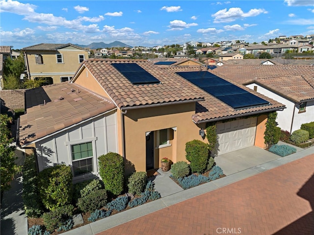 view of front of home with an attached garage, solar panels, a tiled roof, concrete driveway, and a residential view