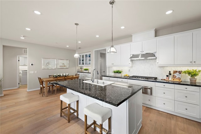 kitchen featuring an island with sink, under cabinet range hood, light wood-type flooring, and tasteful backsplash