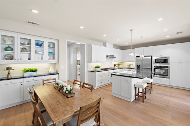 kitchen with a breakfast bar area, dark countertops, light wood-style flooring, appliances with stainless steel finishes, and a sink