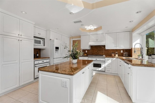 kitchen with white appliances, light tile patterned floors, under cabinet range hood, white cabinetry, and a sink