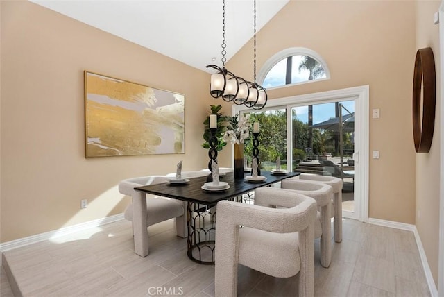 dining space with high vaulted ceiling, light wood-type flooring, an inviting chandelier, and baseboards