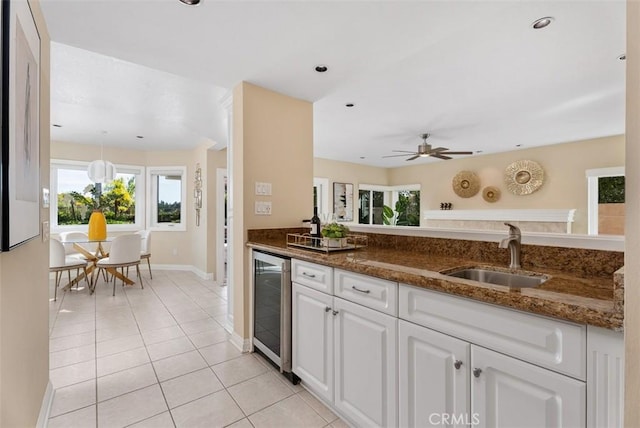 kitchen featuring light tile patterned floors, wine cooler, a sink, white cabinetry, and dark stone countertops