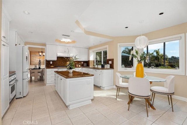 kitchen featuring under cabinet range hood, white appliances, a kitchen island, visible vents, and backsplash