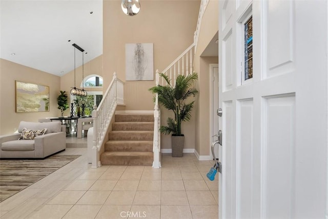 foyer entrance featuring light tile patterned floors, baseboards, stairs, and high vaulted ceiling