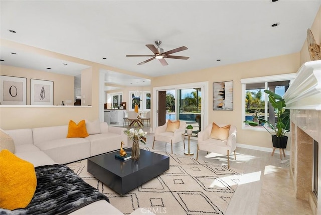 living room featuring a healthy amount of sunlight, baseboards, a ceiling fan, and a high end fireplace