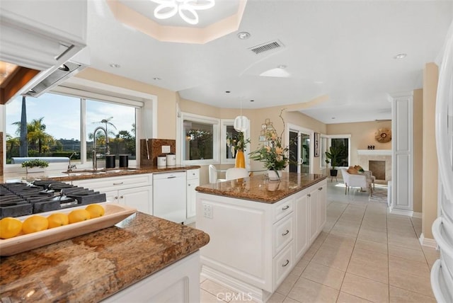 kitchen with white dishwasher, a fireplace, a kitchen island, a sink, and visible vents