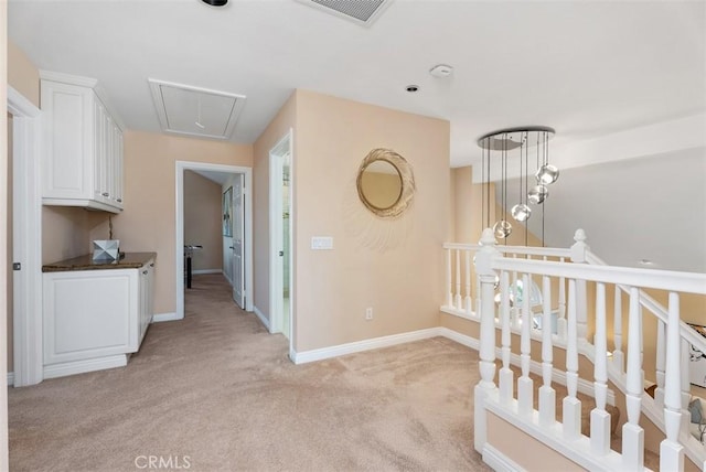 corridor featuring light carpet, attic access, visible vents, and baseboards