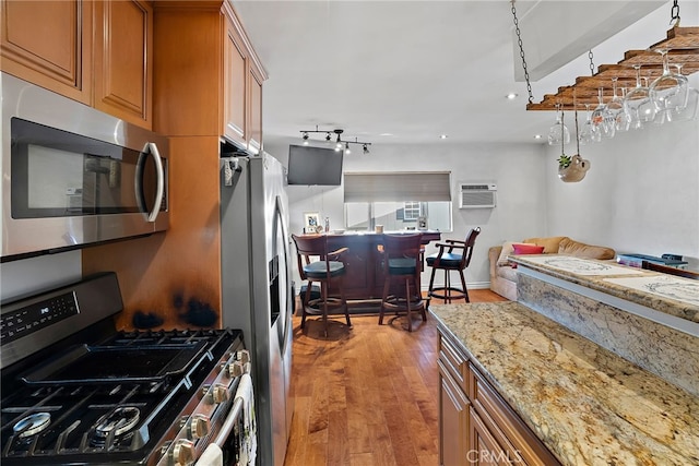 kitchen featuring light wood-style flooring, appliances with stainless steel finishes, brown cabinets, light stone counters, and a wall mounted air conditioner