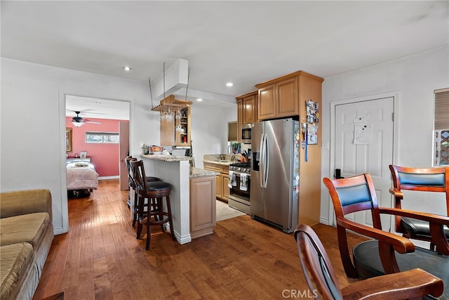 kitchen featuring a breakfast bar, hardwood / wood-style floors, open floor plan, a peninsula, and stainless steel appliances